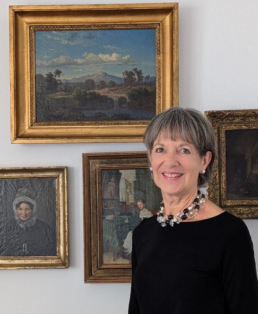 Webseiteninhaberin vor Wand mit gerahmten Gemälden - Kunstsachverständige München